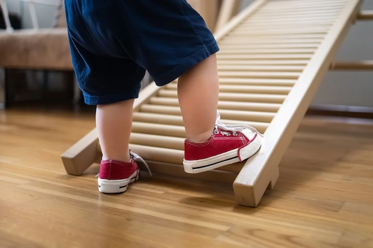 Maluch uprawia sport na ścianie gimnastycznej, nogi w szortach i czerwonych tenisówkach