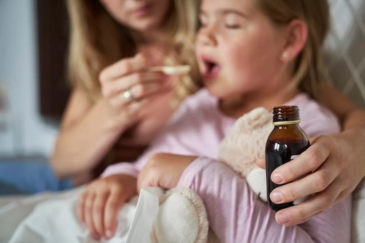Matka podaje syrop chorej dziewczynie w łóżku