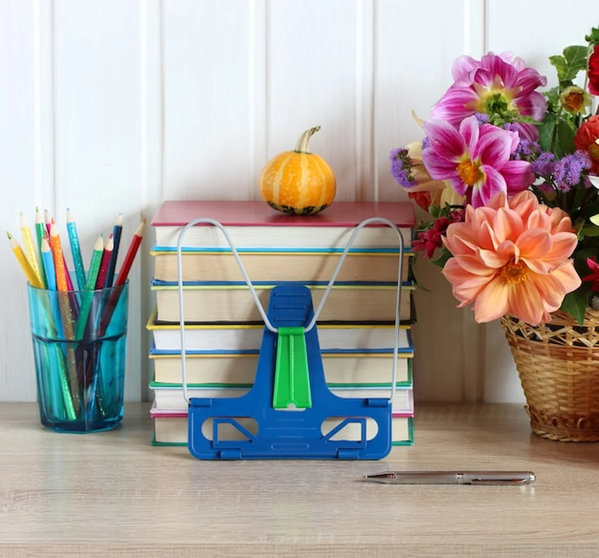 Przybory szkolne na stole: stos podręczników, kredki i bukiet