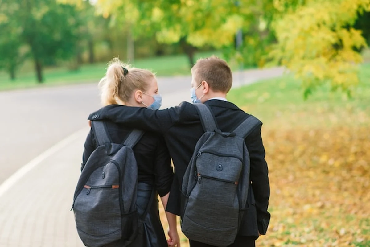 Dzieci w wieku szkolnym w maskach medycznych spacerują po parku miejskim