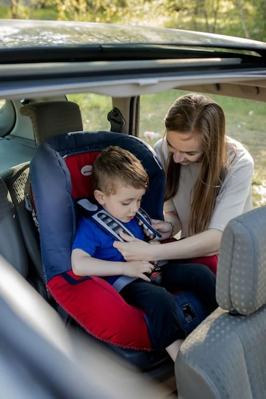 Młoda matka zapinająca syna w foteliku samochodowym