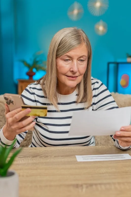 Dojrzała kobieta płacąca rachunki przez smartfona i kartę kredytową