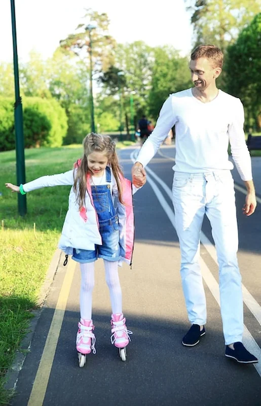 Troskliwy ojciec uczy młodą córkę jeździć na rolkach w parku