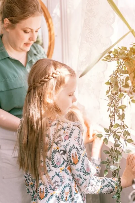 Szczęśliwa matka z córkami bawiąca się na wsi w słoneczny dzień obok okna z roślinami