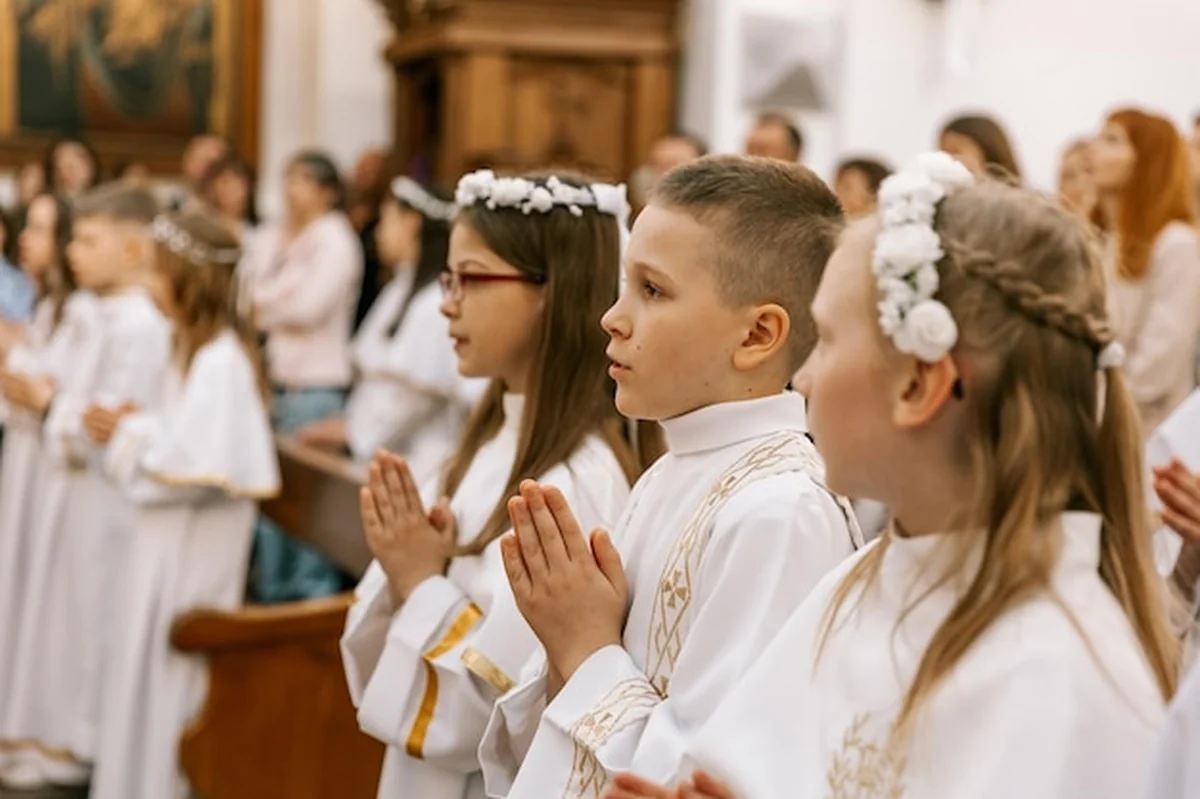 Dzieci przyjmujące pierwszą komunię w kościele katolickim, ksiądz je błogosławi