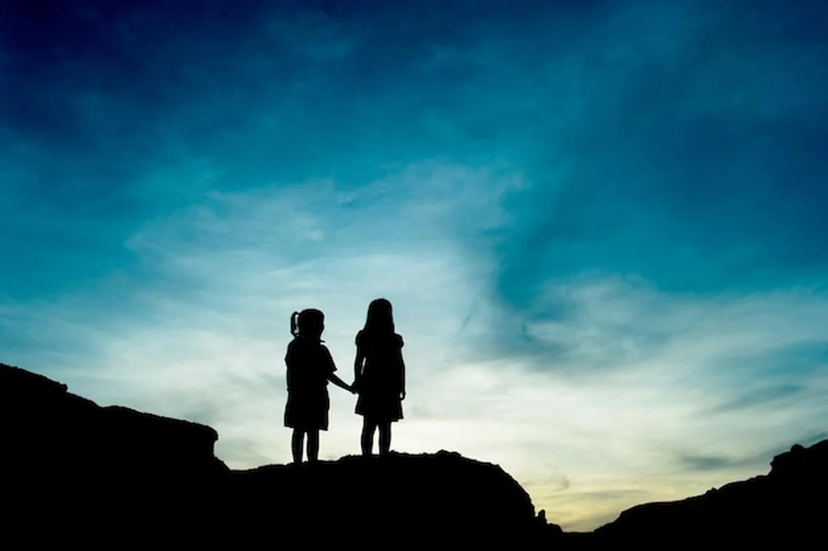 Silhuety rodzeństwa na skale przed niebieskim niebem